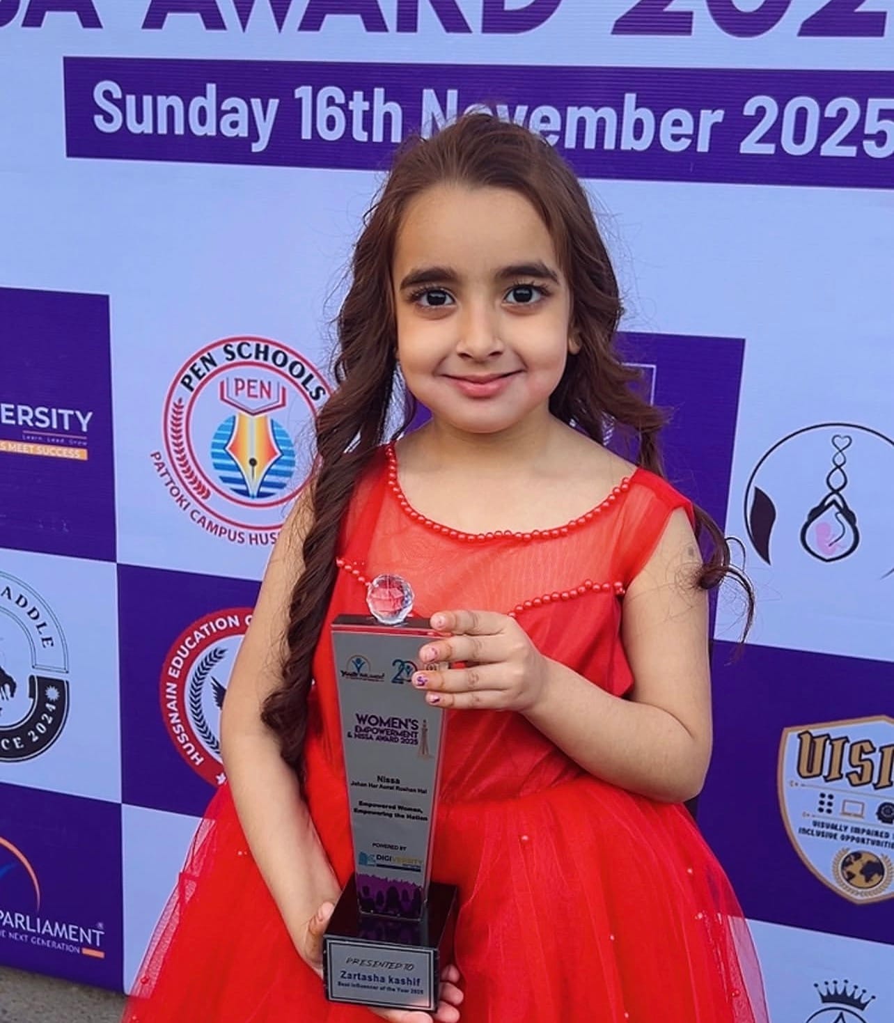 Zartasha Kashif (Tashu) smiling proudly in a vibrant red dress, holding her Best Influencer Of The Year 2025 trophy won at the Youth Parliament Nisa Awards.